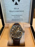Skeleton watch displayed in open presentation box showing care instructions printed on lid