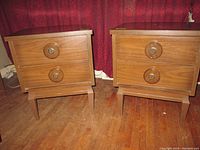 Image of two midcentury modern style bedside tables placed side by side showing drawer fronts with circular wood knobs and tapered legs.