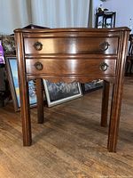 Front view of antique wooden two drawer side table showing detailed wood grain, ring pull hardware, and raised edge.