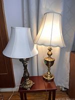 Photo showing two table lamps with white fabric shades sitting on a small reddish-brown wooden side table.