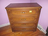 Full front view of the dresser showing four closed drawers, medium brown wood with decorative drawer front details, metal handles, and square legs.