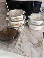 Overview of all casserole dishes showing the vegetable garden and blue cornflower Corning Ware sets along with Pyrex clear glass bakeware.