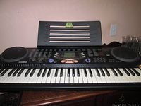 Front view of Casio keyboard showing full 61 keys, speakers on both sides, and music stand attached at back.