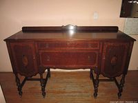 Full view of dark wood credenza with carved doors, central drawers, and wheels on turned legs.