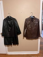 Two leather jackets and a leather skirt hanging on wall, showing whole lot
