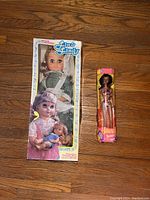 Photo showing Lin & Lindy doll in original packaging alongside Teresa Barbie doll in original packaging on wooden floor.