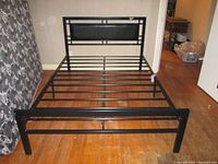 Photo showing black metal double bed frame with geometric headboard and slatted base without mattress.