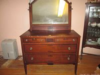 Full view of wooden dresser with attached mirror. Three large drawers at the bottom and three smaller upper drawers with metal handles and decorative inlays.