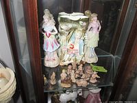 Porcelain figurines and decorative vase displayed in glass cabinet