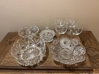 Overview of all glassware on table including four wine glasses and five serving/candy dishes showing clear glass with detailed cut designs.