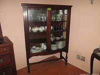 Full view of wooden dishware hutch with glass doors and contents inside for visual reference. Positioned against wall on hardwood floor.