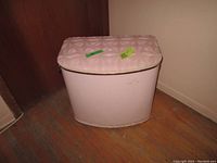 Side view of pink metal laundry hamper showing soft patterned lid and solid body with some discoloration at bottom.