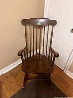 Front view of the wooden rocking chair showing the curved top rail, spindle back, and armrests