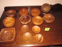 Top down view of 11 wooden serving dishes arranged on a wooden surface including round bowls, scoops, and a square dish.