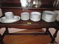 Four stacks of porcelain plates and bowls arranged on a wooden shelf, showing different sizes and quantities of plates and bowls.