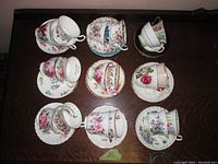 Top view of nine teacups with matching saucers, arranged on a wooden surface, showing floral designs and gold trim