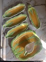 Top view of the full set showing 4 corn holders, 1 butter boat, and the serving dish, on a marble surface with natural lighting.