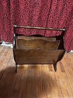 Front view of the wooden magazine rack showing its compartments, dark brown finish, and bamboo-style horizontal handle.