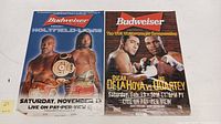 Two boxing match posters side by side on a white surface, showing fighters Holyfield vs Lewis on the left and De La Hoya vs Quartey on the right.
