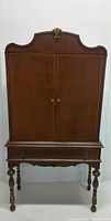 Front view of wooden highboy style china cabinet with decorative top and closed two doors
