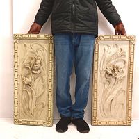 Full-length image showing person holding both rectangular molded resin 3D wall plaques with floral designs and decorative borders, displaying size and scale.