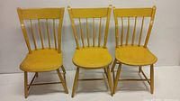 Front view of three yellow painted antique farmhouse chairs with plank seats against white background.