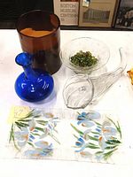 Photo showing all five items grouped together including the cobalt blue vase, amber vase, clear glass horn-shaped cornucopia, small glass bowl with marbles, and floral fused glass dish.