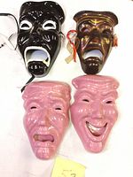 Four theater masks: two ceramic pink comedy and tragedy masks, two metal black and bronze masks.