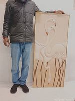 Man holding the framed textile art featuring three flamingos, showing size and scale.