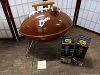 Photo of Coors branded football-shaped hibachi grill with two NSync 2001 bobbleheads in original Best Buy packaging next to it