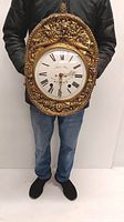 Person holding the ornate golden enameled wall clock showing full front view
