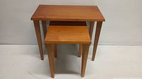 Front view of the pair of wooden nesting tables stacked with smaller under larger.