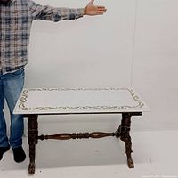 Front angle view showing the full rectangular white marble tabletop with gold scroll border and the carved claw feet wooden legs connected by a turned stretcher.
