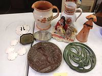 Overview of the lot showing entire collection on a white table including pottery pitcher, Native American figurine, Moses plaque, sand dollar ceramic pieces, and other decor items.