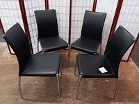 Set of four black modern dining chairs arranged in a circle, showing overall look and style.