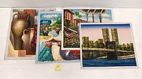 Four signed oil paintings on canvas showing various themes laid flat on a white table.