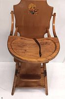 Full front view of vintage wooden child's highchair showing tray, strap, arms, and wooden seat with illustration on backrest.