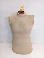 Front-facing photo of the beige fabric dress form showing its shape, fabric texture and wooden neck block on top.
