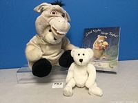 Build-A-Bear donkey plush, baby bear plush, and book placed against blue background
