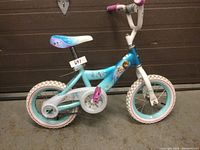 Right side view of blue and white girls bicycle with Frozen graphics, showing front and rear tires, pink pedals and seat.
