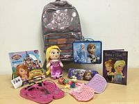 Photo showing the overall contents of the lot with backpack, lunch kit, flip flops, dolls, book, and accessories arranged on a surface.