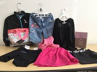 Full lot laid out on table showing jacket, denim shorts, pink skirt, black top, sweatpants, Crocs, tote bag, and devotional book.