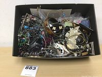 Box with mixed jewelry items including necklaces, bracelets, earrings, and a watch packed together.