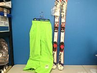 Full view of neon green children's ski pants size 11-12 with Rossignol junior skis.