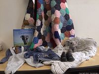 Full lot view showing quilted throw, baby sleep sack, elephant book, hoodie, shoes, and blanket on surface