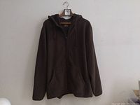 Full view of brown hoodie hanging on hanger, showing front, zippered, pockets, and hood.