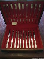 Closed flatware box showing full set of 20 pieces including forks, spoons, and knives, arranged neatly on a red fabric interior.