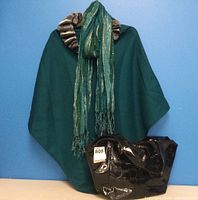 Full view of teal cape, green metallic scarf, and black patent leather purse against blue background