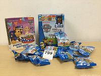 Full lot image showing 10 individually packaged Paw Patrol Micro Lites mini figures displayed beside a blue display box with Paw Patrol branding and a separate story book box (not included).