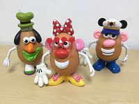 Three Mr. Potato Head toys styled after characters Goofy, Lady, and Sea Captain placed side by side on a table.